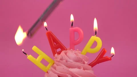 The inscription Happy with burning multi-colored candles on a cupcake on a pink Stock Footage 274670215