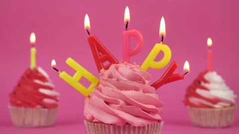 The inscription Happy with burning multi-colored candles on a cupcake on a pink Stock Footage 275145217