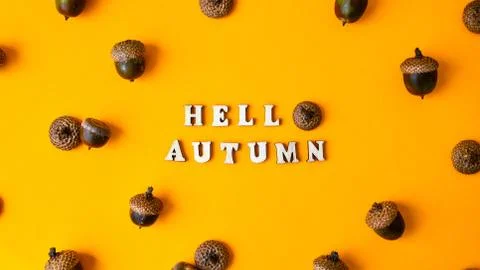 Inscription HELLO AUTUMN text Pattern with acorns on the yellow background. A Stock Photos