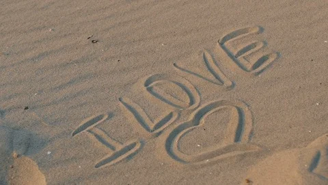 The inscription on the sand "I love", on which the foot steps. close - up, slow Stock Footage 91563243