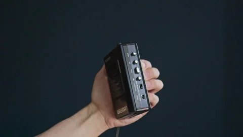 Inserting an audio cassette into a vintage Walkman and pressing play Stock Footage 306539572
