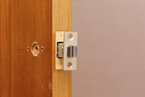 Inserting door latch in end hole close-up. Fitting door lock in panel. Markup Stock Photos