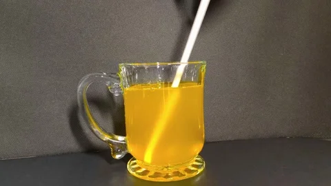 Inserting straw into a clear glass cup of orange juice with a handle on a d.. Stockbeeldmateriaal 318125044
