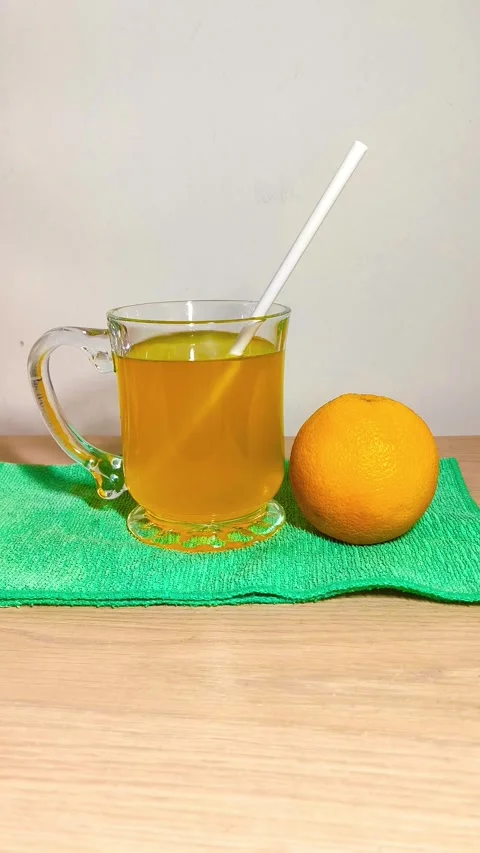 Inserting straw in a clear glass cup of orange juice with a handle on a green Video stock 318125507