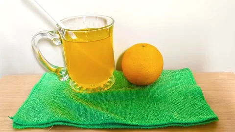 Inserting straw into a clear glass cup of orange juice with a handle on a g.. Video stock 318125617