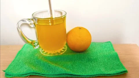 Inserting straw into a clear glass cup of orange juice with a handle on a g.. Stock Footage 318125700