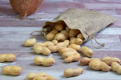 Inshell peanuts fell out of a linen bag against a wooden background Stock Photos