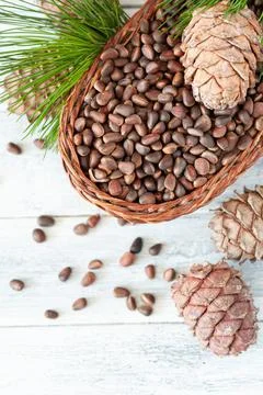 Inshell pine nuts in a wicker basket. Nearby are nuts, pine cones and needles Stock Photos