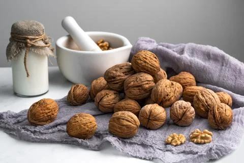 Inshell walnuts, a bottle of milk and a mortar with nuts, on a gray napkin, w Stock Photos