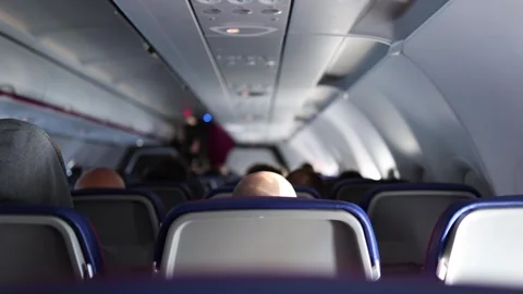 Inside airplane cabin rows of passengers sit quietly under soft ceiling lights h Stock Footage 310856647