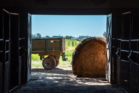Inside a barn looking outside, with a hay roll or bale and a truck trailer wi Stock Photos