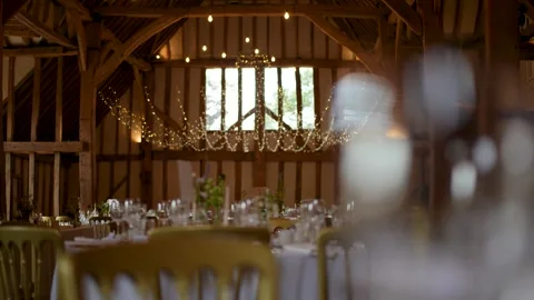 Inside a barn that is set up for a wedding breakfast with glasses and tables Stock Footage 293809212