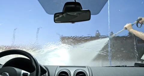 Inside car view washing soapy windshield with high pressure jet spray Stock Footage 338338616