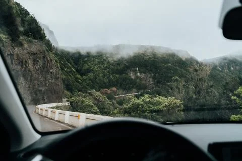 Inside car view winding road through lush green mountains with fog on a cloudy Foto stock
