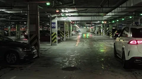 Inside dark half-occupied underground parking lot, black car drives away in Stock Footage 314888378