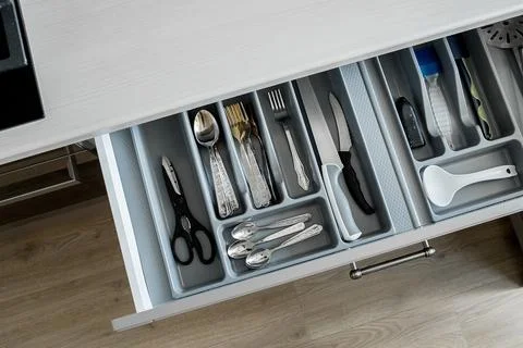 Inside the drawer, a variety of kitchen utensils, including forks, spoons, and k Stock Photos