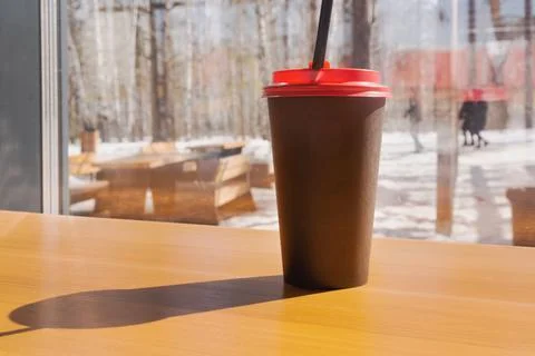Inside the forest cafe, there is coffee in a black paper cup on a wooden tabl 스톡 사진