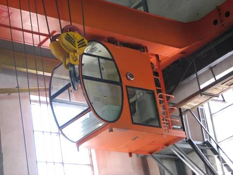 Inside an industrial building, an orange overhead crane cabin is suspended .. Stock Photos