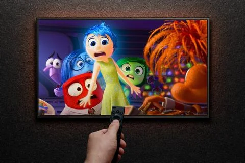 Inside Out 2 trailer or movie on TV screen. Man turns on TV with remote control. Stock Photos