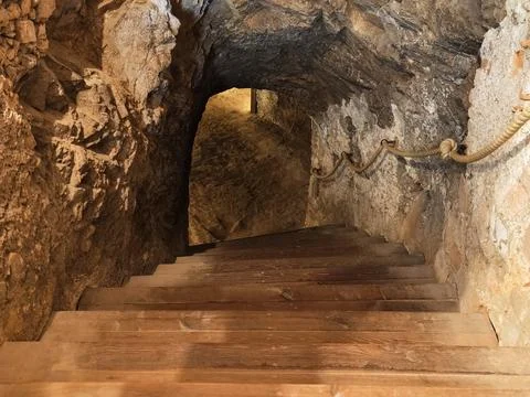Inside rugged cave tunnel with rough stone walls, arched ceiling, wooden st.. Stock Photos