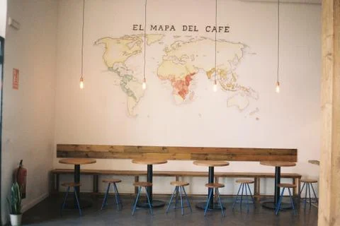 An inside shot of a cafe with round tables and chairs near a map of coffee pr Stock Photos