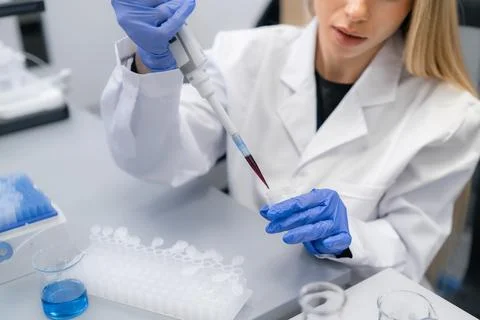 Inside a sterile laboratory environment, technician pipetting red liquid into Foto stock