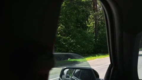 Inside of a vehicle with a side mirror reflecting a winding road. Trees line the Stock Footage 345868687