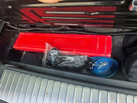 Inside a vehicle's storage compartment, a bright red tool rests beside a blue Stock Photos