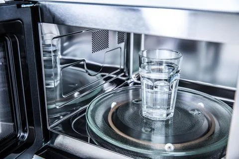 Inside view of new clean staniless, microwave oven with a cup of pure water Stock Photos