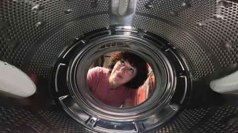 Inside view of washing machine drum showing woman curiously looking in Stockbeeldmateriaal 294946404