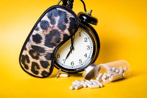 Insomnia concept. Alarm clock, leopard sleep mask and sleeping pills with yel Stock Photos