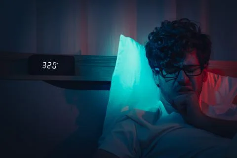 Insomnia sleepless man having a problem sleeping in late night with alarm clo 库存照片