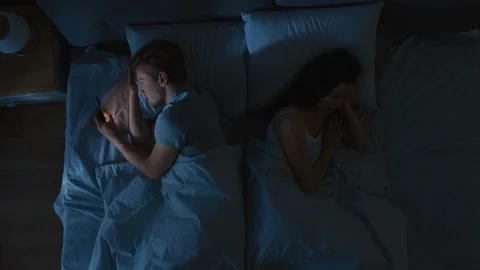 Insomniac Stressed Young Man Uses Smarphone at Night in Bed Girlfriend Sleep Stock Footage