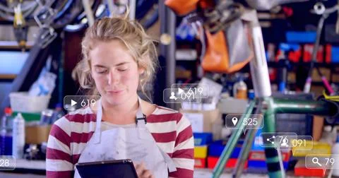 Inspecting mechanic in apron using tablet in bike shop with hanging wheels tools Stock Photos