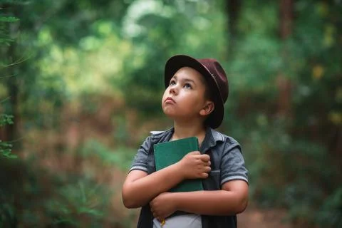 Inspired boy hugging a book looking up in a forest. Foto stock