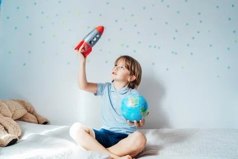 Inspired boy playing with space rocket and planet Earth models sitting on the Stock Photos