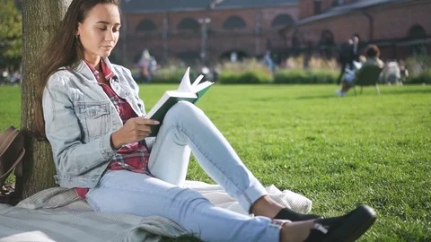 Inspired university student reading book sitting on campus grass. Stock Footage 101795929