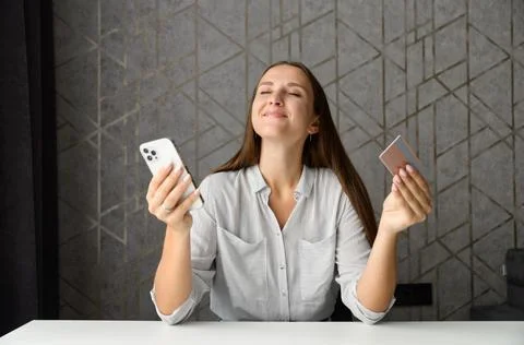 Inspired woman holding credit card and smartphone imagines long awaited Stock Photos