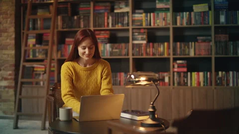 Inspired young female author types on laptop in library, working on new book Stock Footage 342731535