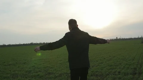 Inspired young man turning with outstretched arms in the green grass field at Видео 106316091