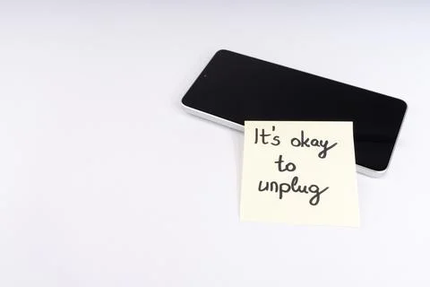 Inspiring 'It's Okay to Unplug' message on a sticky note next to a smartpho.. Stock Photos