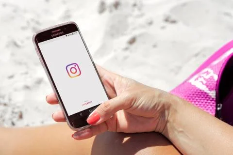 Instagram app opening. Woman in the beach with a mobile phone in her hands. Stock Photos