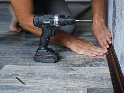 Installation of a brown wooden baseboard in a room with a gray interior Stock Photos