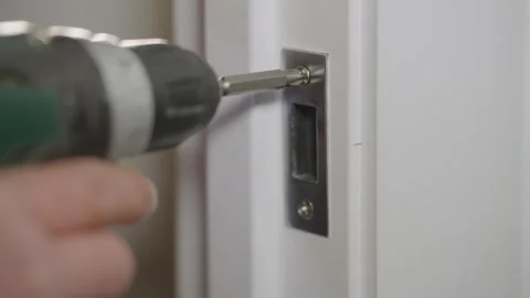 Installation of the door lock striker. Screwdriver screws the screw Stock Footage 331237539