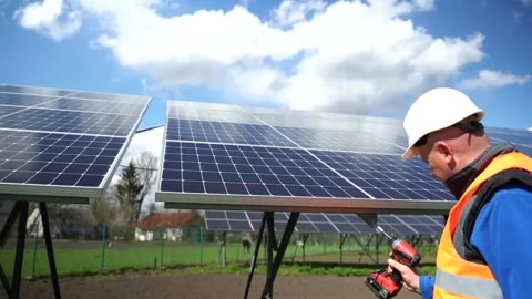 Installation of solar panels at a power plant. Man with a drill fixing solar Stock Footage 168178458