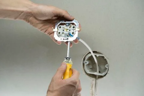Installation wire into a plug. A man installs an electrical outlet in the wal Stock Photos