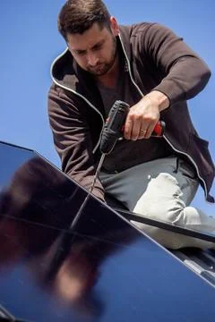 Installer fixing solar panel with a cordless drill on a residential house roo Stock Photos