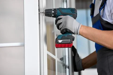 Installer in overalls automatic screwdriver in hands and installs plastic door Stock Photos