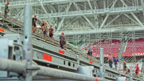 Installers in helmets construct assembling frame for tribune Stock Footage 234425795