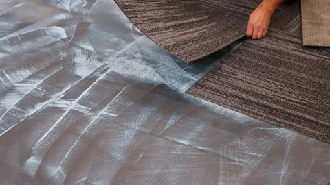 Installing carpet tiles on an adhesive surface in modern interior Stock Footage 337497476
